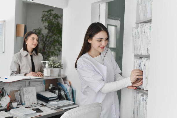Healthcare worker organizing patient files on a shelf in a medical office.