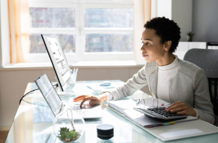 Businesswoman working at a desk, using a calculator and computer to analyze financial data.