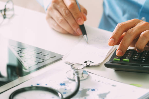 Person calculating medical costs with a stethoscope and charts on the desk.