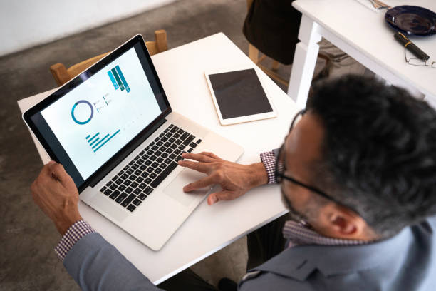 Man reviewing business charts and graphs on a laptop at a desk.