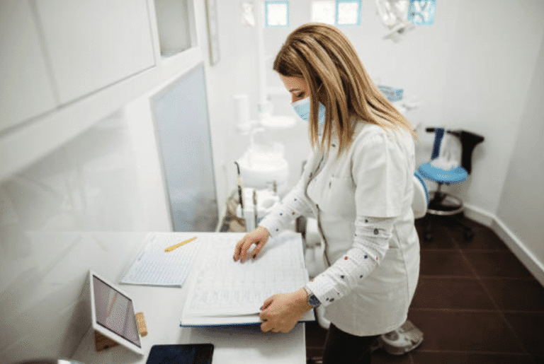 Dental professional wearing a mask reviewing a large open ledger in a clinic.