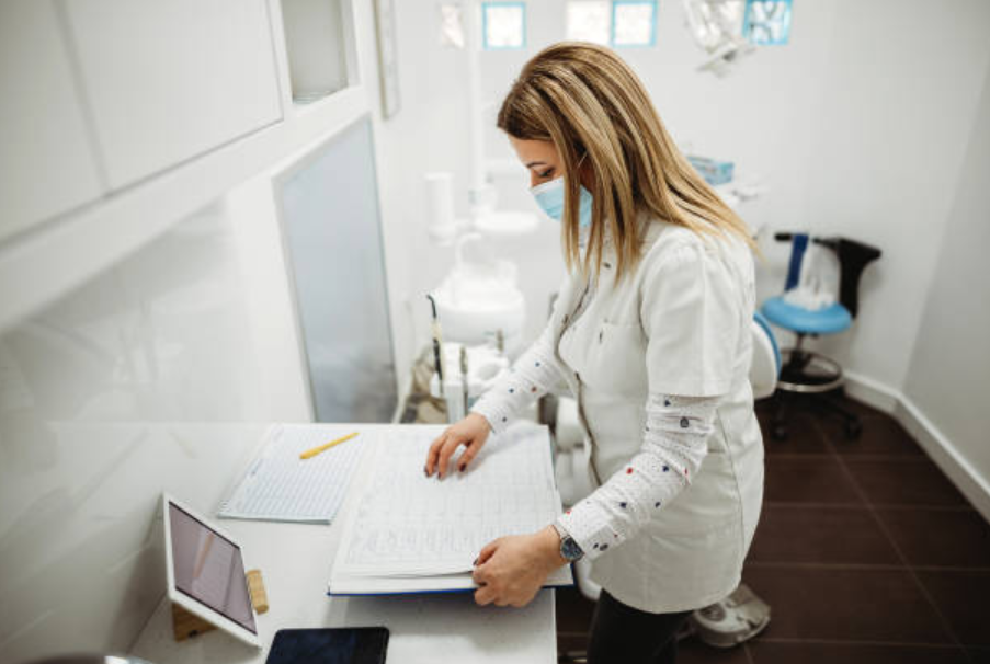 Dental professional wearing a mask reviewing a large open ledger in a clinic.