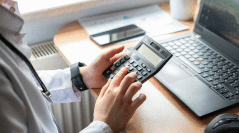 Person using a calculator at a desk with a laptop and documents.
