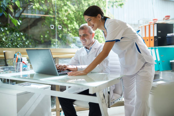Two healthcare professionals smiling while looking at a laptop in a bright office.