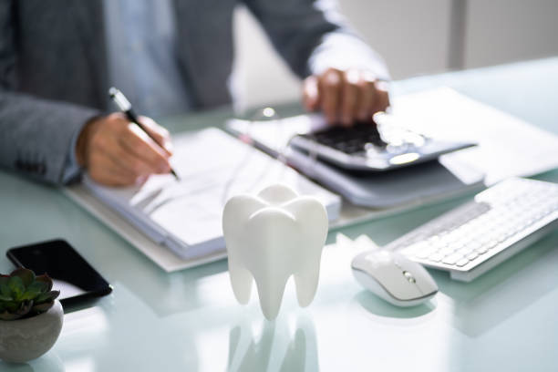 Close-up of a desk with a tooth model, keyboard, and person writing in a notebook