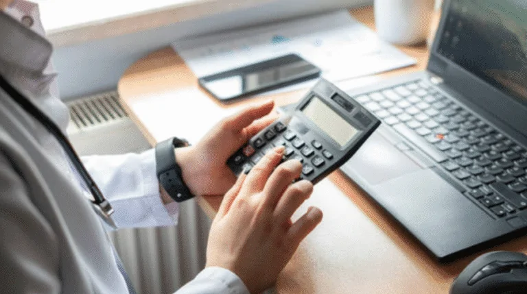 Person using a calculator at a desk with a laptop and documents.